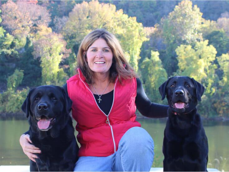 Smiling Loretta Rocco, owner and trainer of The Positive Pooch, with two black labs by her sides
