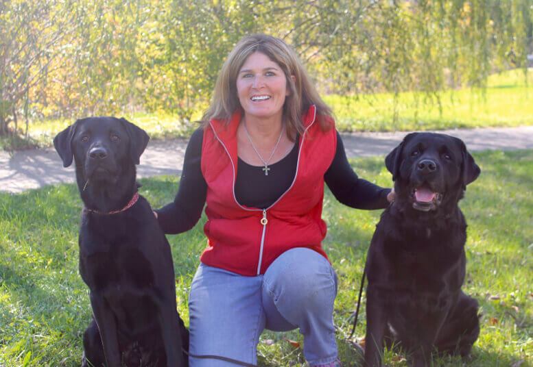 Smiling Loretta Cleveland, owner and trainer of The Positive Pooch, with two black labs by her sides
